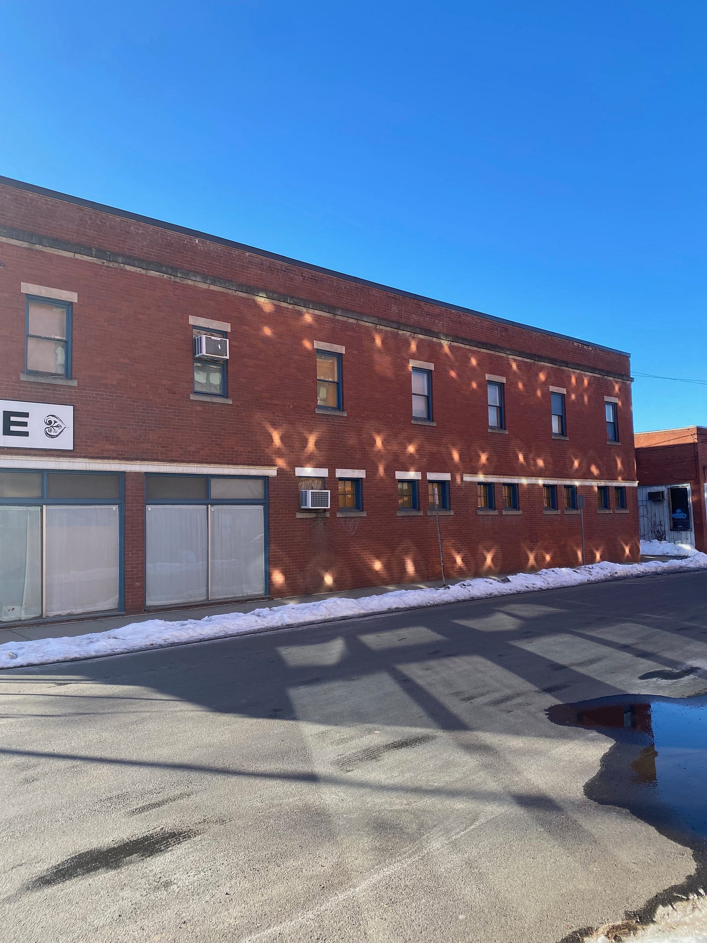 A brick building under a bright blue sky. The building is lit up with small crosses of golden light, reflections from another building.