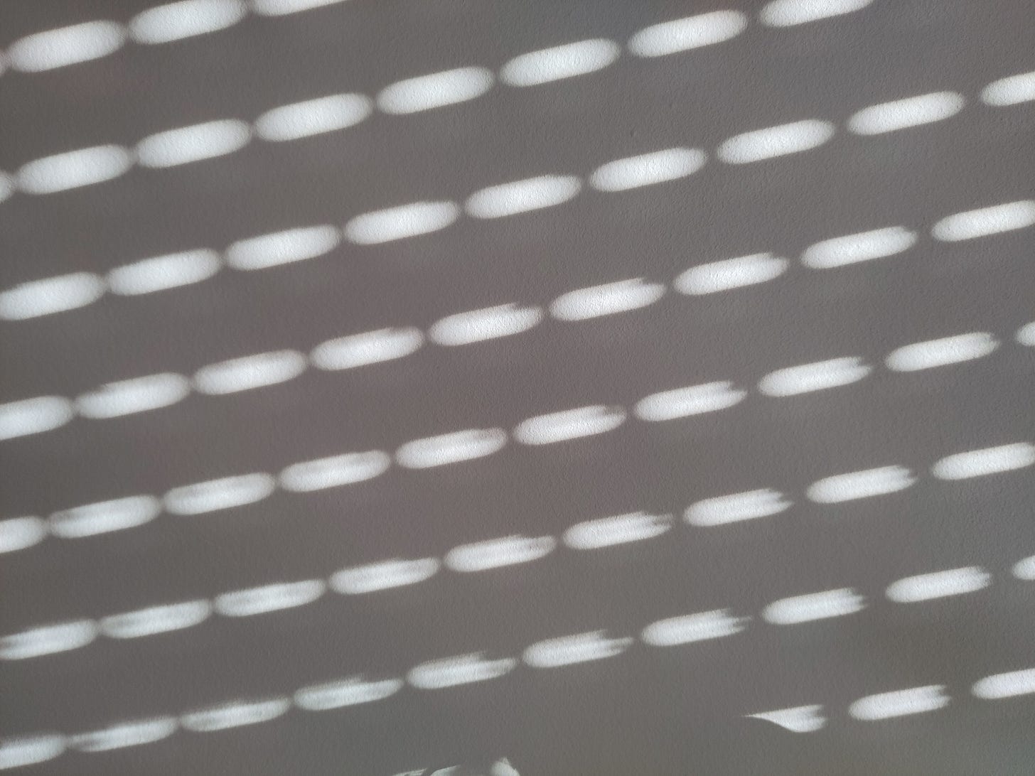 Fotografia di un muro bianco su cui batte la luce che filtra da una serranda