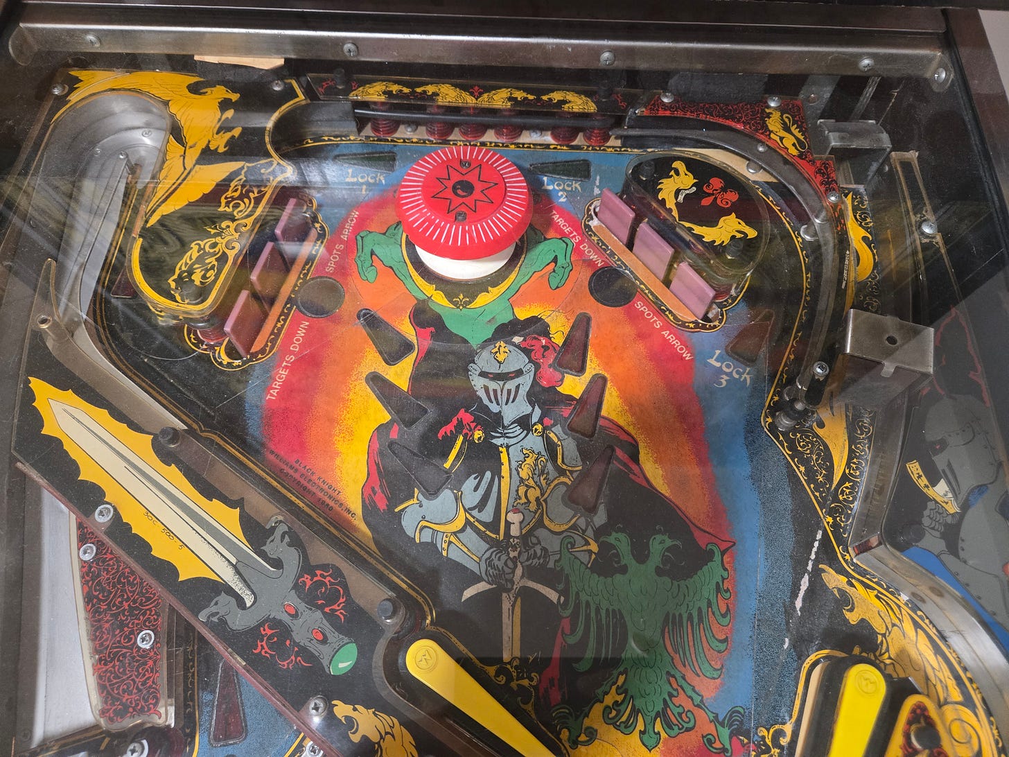 Overhead view of the Black Knight (1980) playfield showing the two-level layout with Lock shots, ramps, sword targets, and knight artwork Overhead view of the Black Knight (1980) playfield showing the two-level layout with Lock shots, ramps, sword targets, and knight artwork
