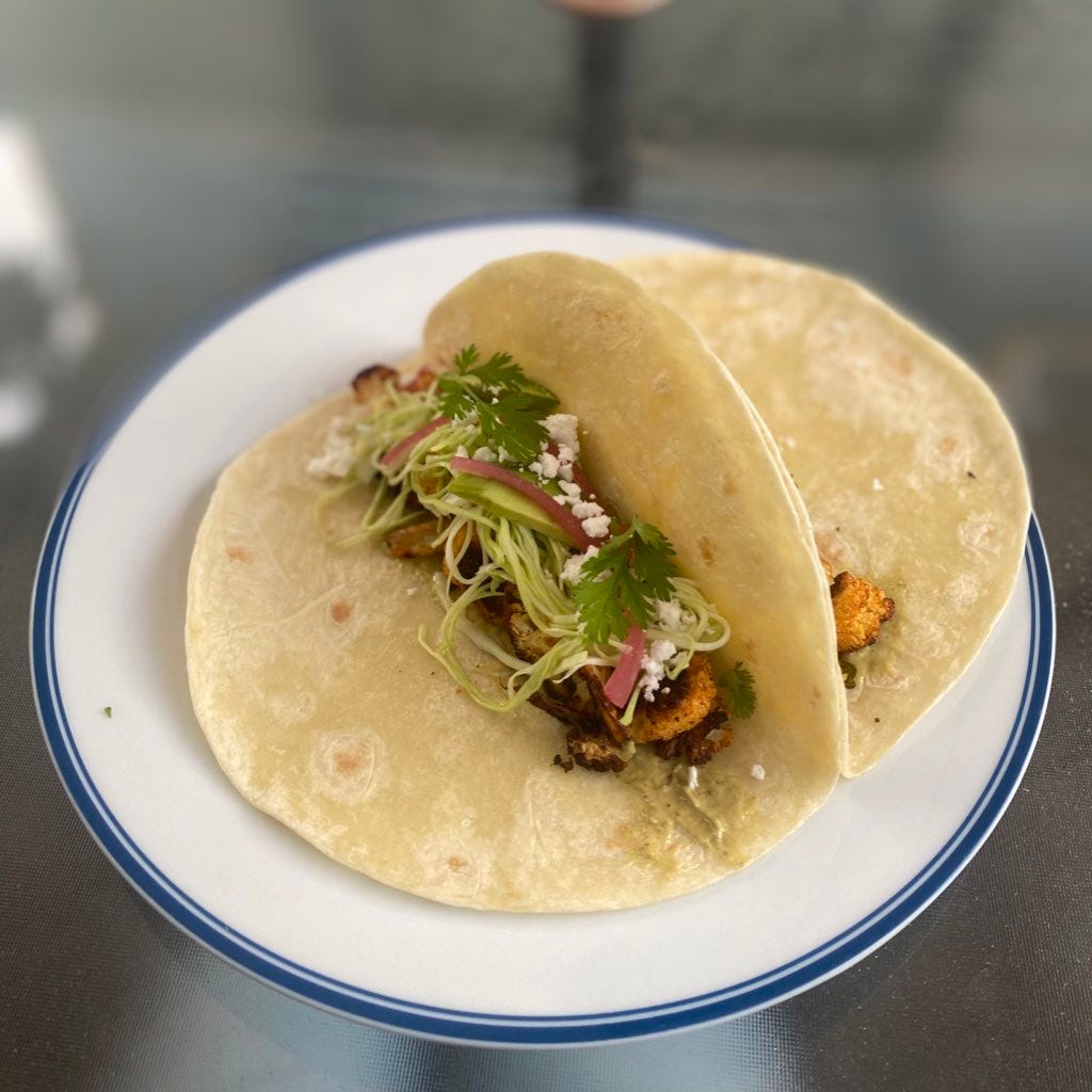 two flour tortillas filled with roasted cauliflower, green cabbage slaw, pickled red onion, avocado, cilantro, and crumbles of feta.