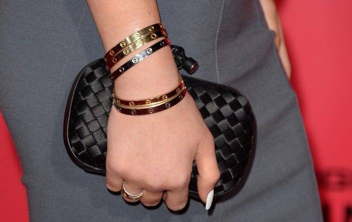 Kylie Jenner's hand with multiple bracelets, a ring, and a black clutch.