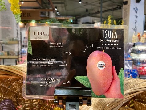 Signs and displays of unusual mango varieties at a grocery store in northern Thailand, including Megumi and Tsuya mangos.