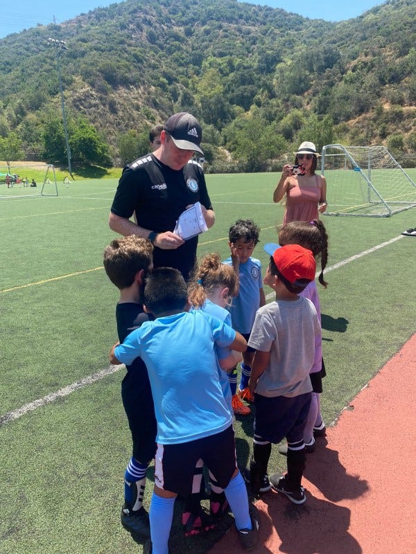 professional soccer coach teaching children how to play soccer. Coach is with a group of 4year olds in their soccer class