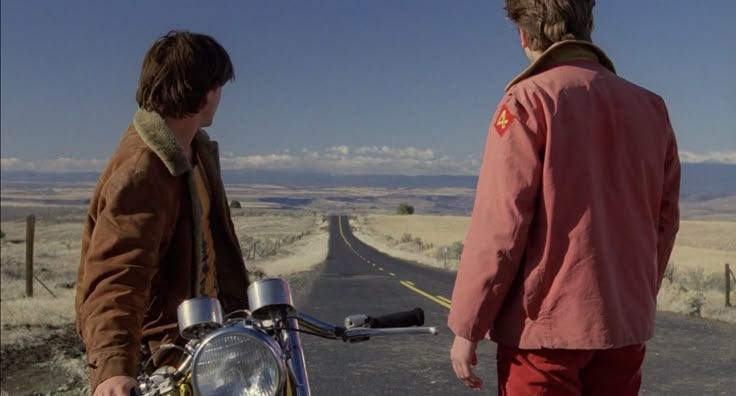 This may contain: two men standing next to each other on the side of a road with a motorcycle