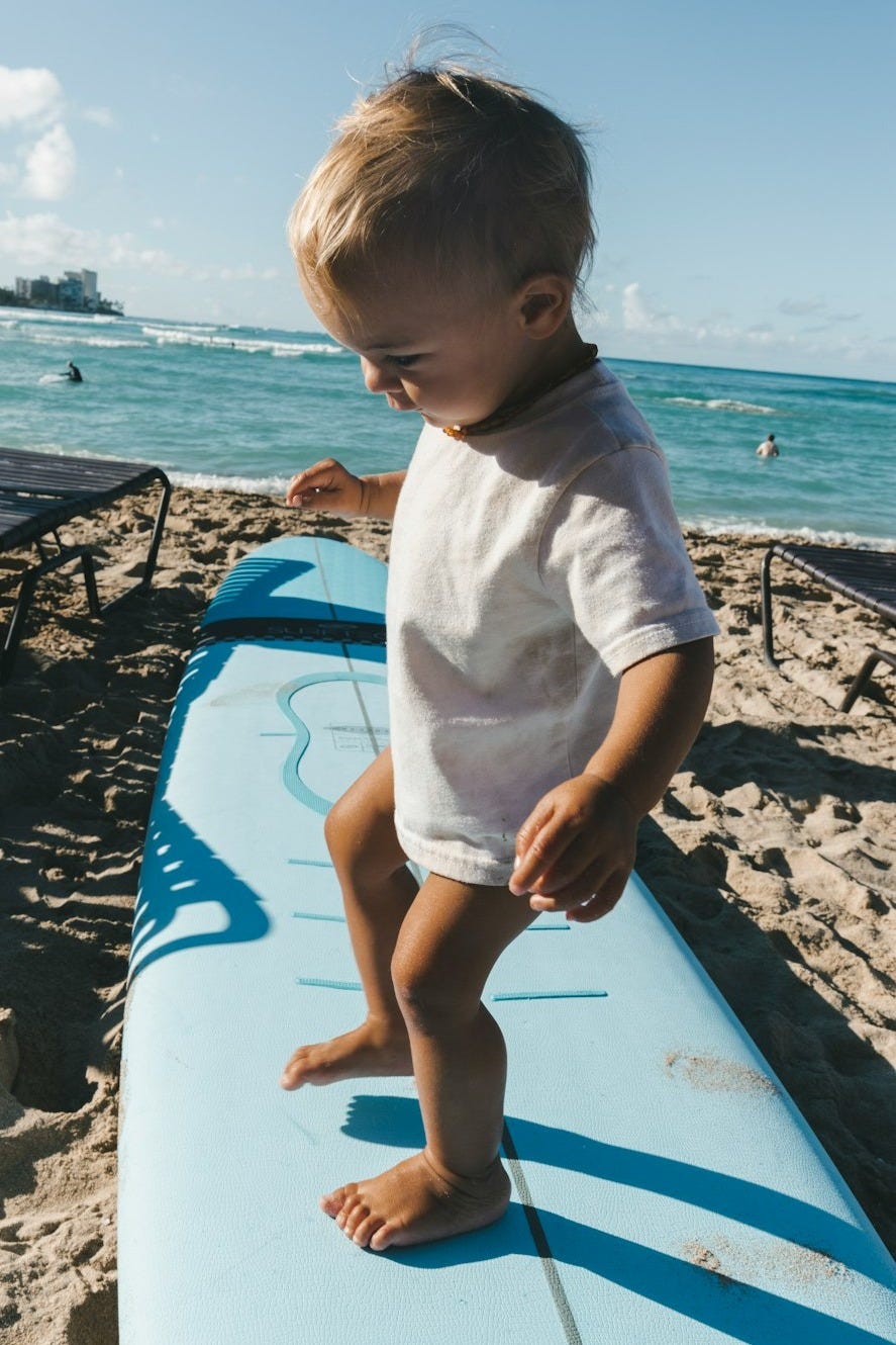 a baby standing on a surfboard on the beach