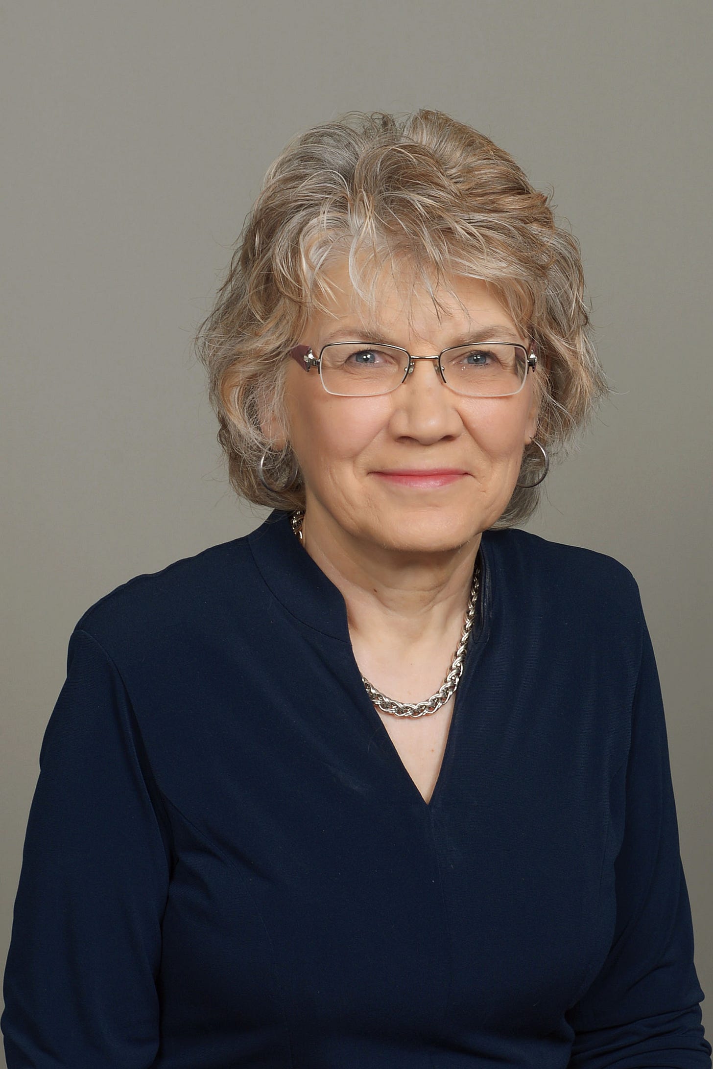 A studio portrait of Linda Camp, a senior woman with short blonde-gray hair and glasses. A studio portrait of Linda Camp, a senior woman with short blonde-gray hair and glasses.
