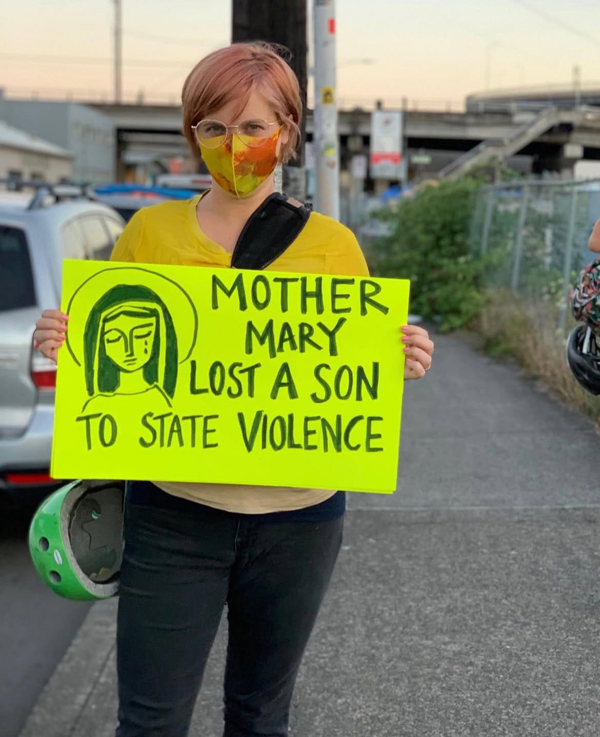 a person with glasses and reddish hair holds up a sign that say mother mary lost a son to state violence