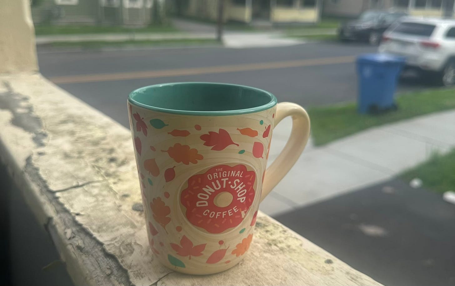 a coffee cup on the railing of a porch of an older house overlooking an urban street