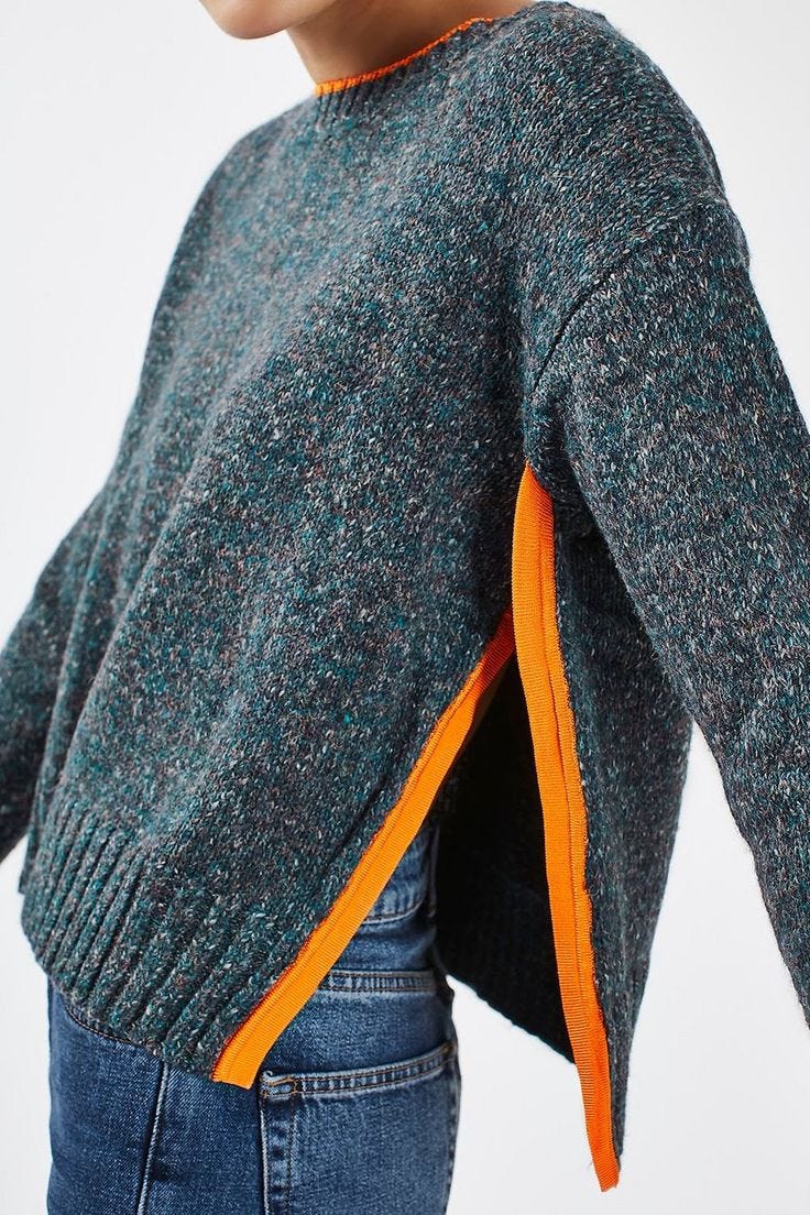 This may contain: a woman is wearing a sweater with an orange stripe on the side and she has her hands in her pockets This may contain: a woman is wearing a sweater with an orange stripe on the side and she has her hands in her pockets