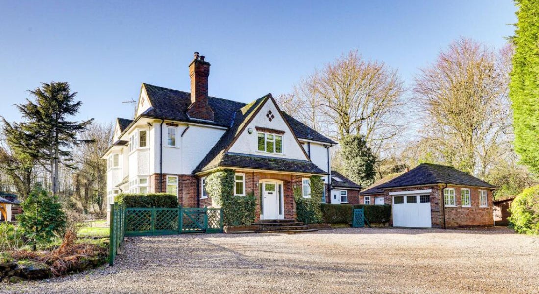 A white and brick house with a green fence in front of it and a blue sky above it A white and brick house with a green fence in front of it and a blue sky above it