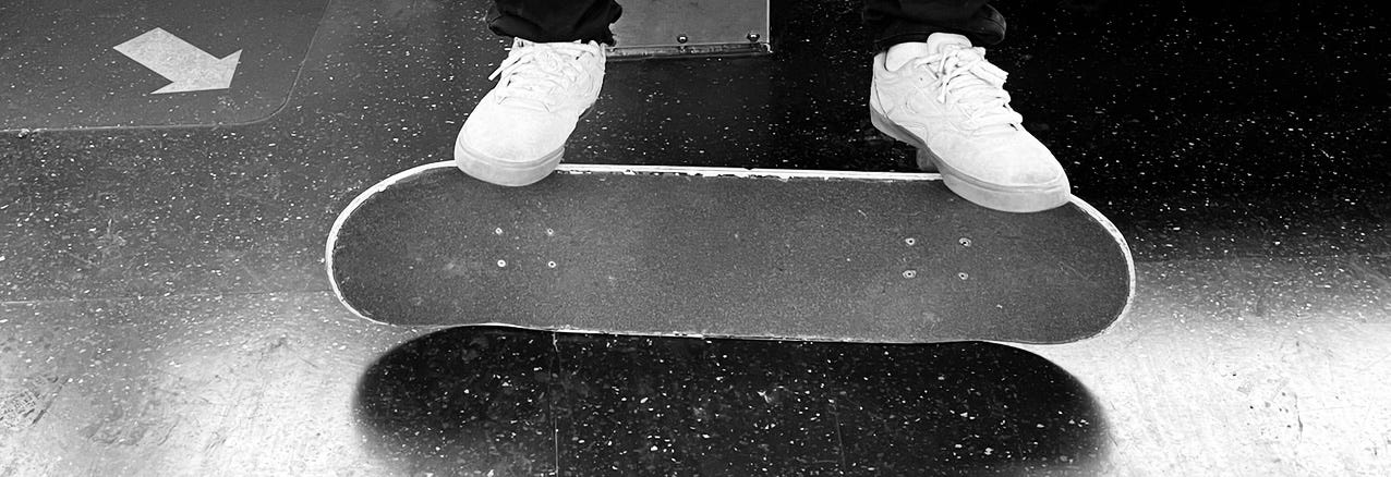 black and white photo of two feet resting on sideways skateboard on the subway train