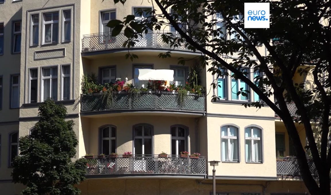 Photo of three floors of a midsized apartment building. Each floor's corner apartment has a large balcony with plants, very cozy looking. The balcony in the center has solar panels discreetly mounted on it, behind the mesh of its railing. Photo of three floors of a midsized apartment building. Each floor's corner apartment has a large balcony with plants, very cozy looking. The balcony in the center has solar panels discreetly mounted on it, behind the mesh of its railing.