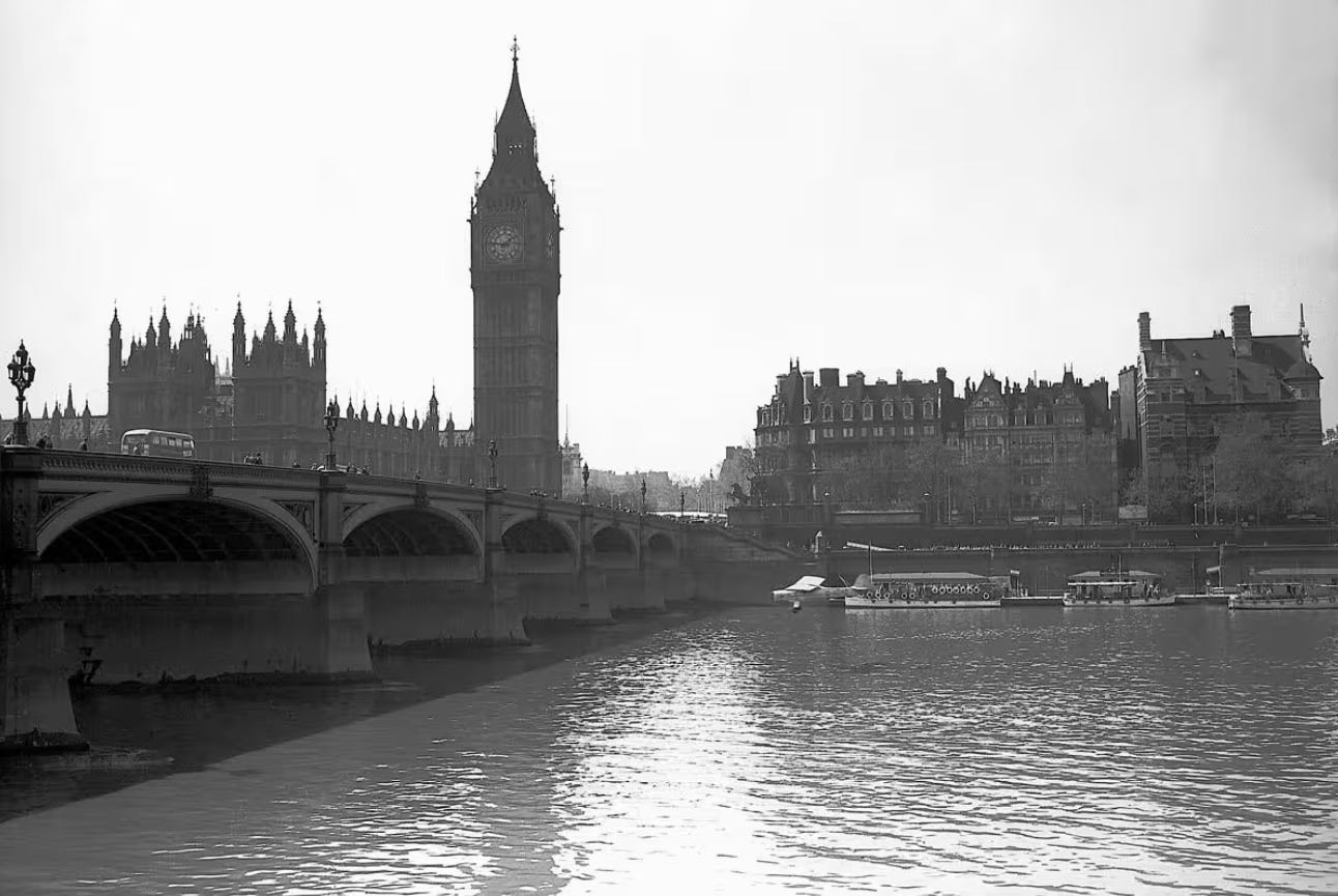 b/w photo of the Palace of Westminster across the Thames. In the middle of the shot, however, is a tiny plane, flying dangerously close to the water, and apparently planning to fly under one of the bridge’s arches. It is clearly being piloted by a lunatic