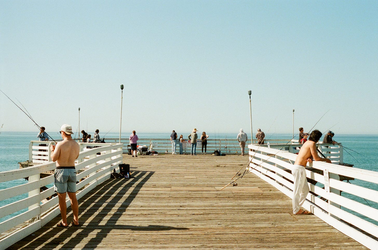 Pacific Beach pier with men fishing and tourists watching surfers and admiring the ocean on a sunny day