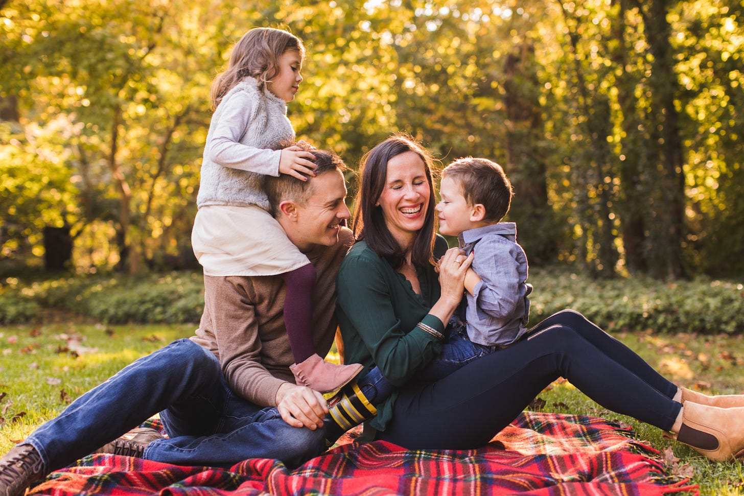 A family sitting and laughing together on a blanket in their backyard.