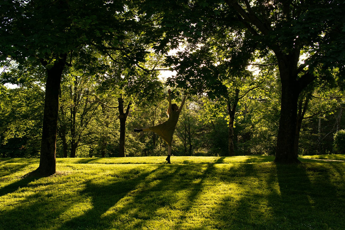 a woman dances in a park surrounded by lush trees and green grass a woman dances in a park surrounded by lush trees and green grass