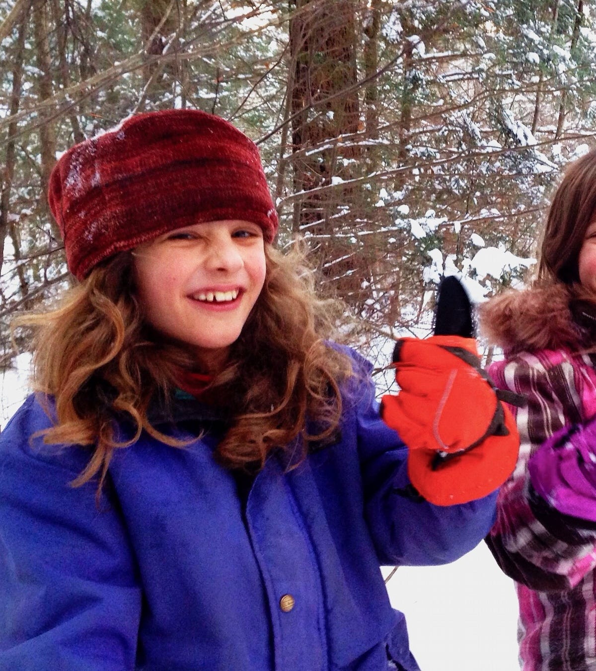 a child of ten or so in the woods in winter. he is wearing colorful clothes and doing a thumbs-up.