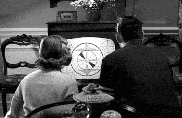 a man and a woman are sitting in front of a television with a clock on it