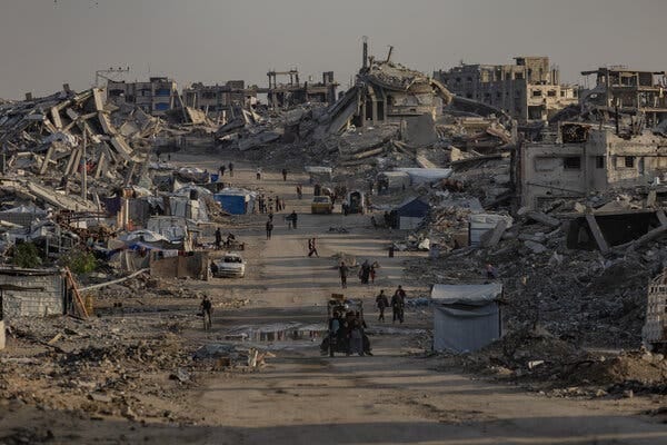 A dirt road running between destroyed buildings, with people and vehicles.