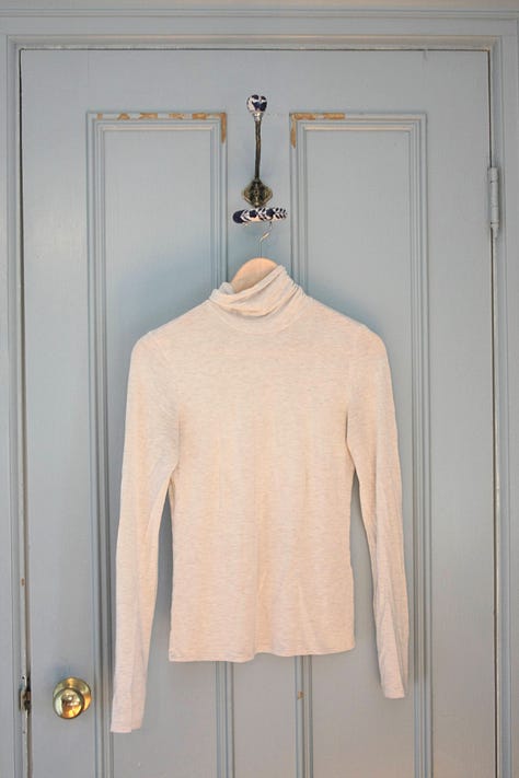 Five shirts, from left to right a white shirt, green turtleneck, oatmeal turtleneck, white t-shirt, and brown turtleneck