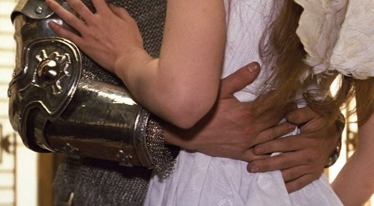 This may contain: a man and woman embracing each other in medieval dress with armor around their necks, both dressed in white