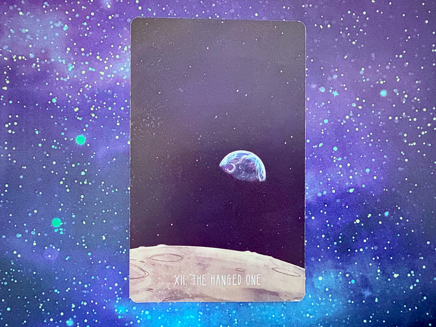 A version of The Hanged One card, illustrated with a painted version of the famous "Earthrise" photo from NASA