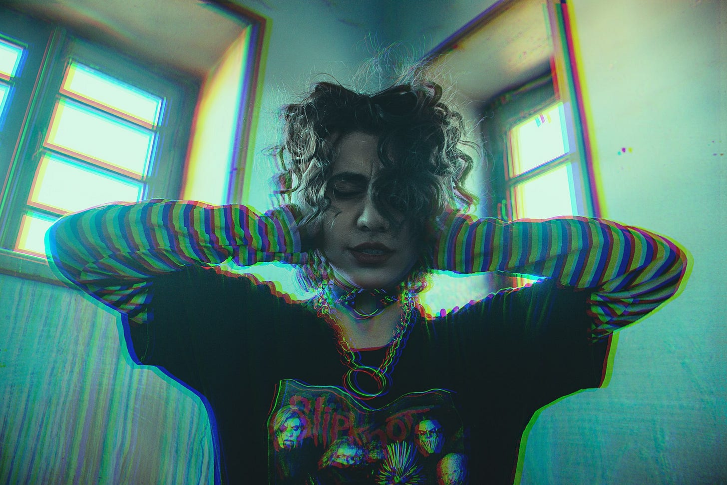 Woman in black and blue-striped shirt in a bright room, hands over ears.