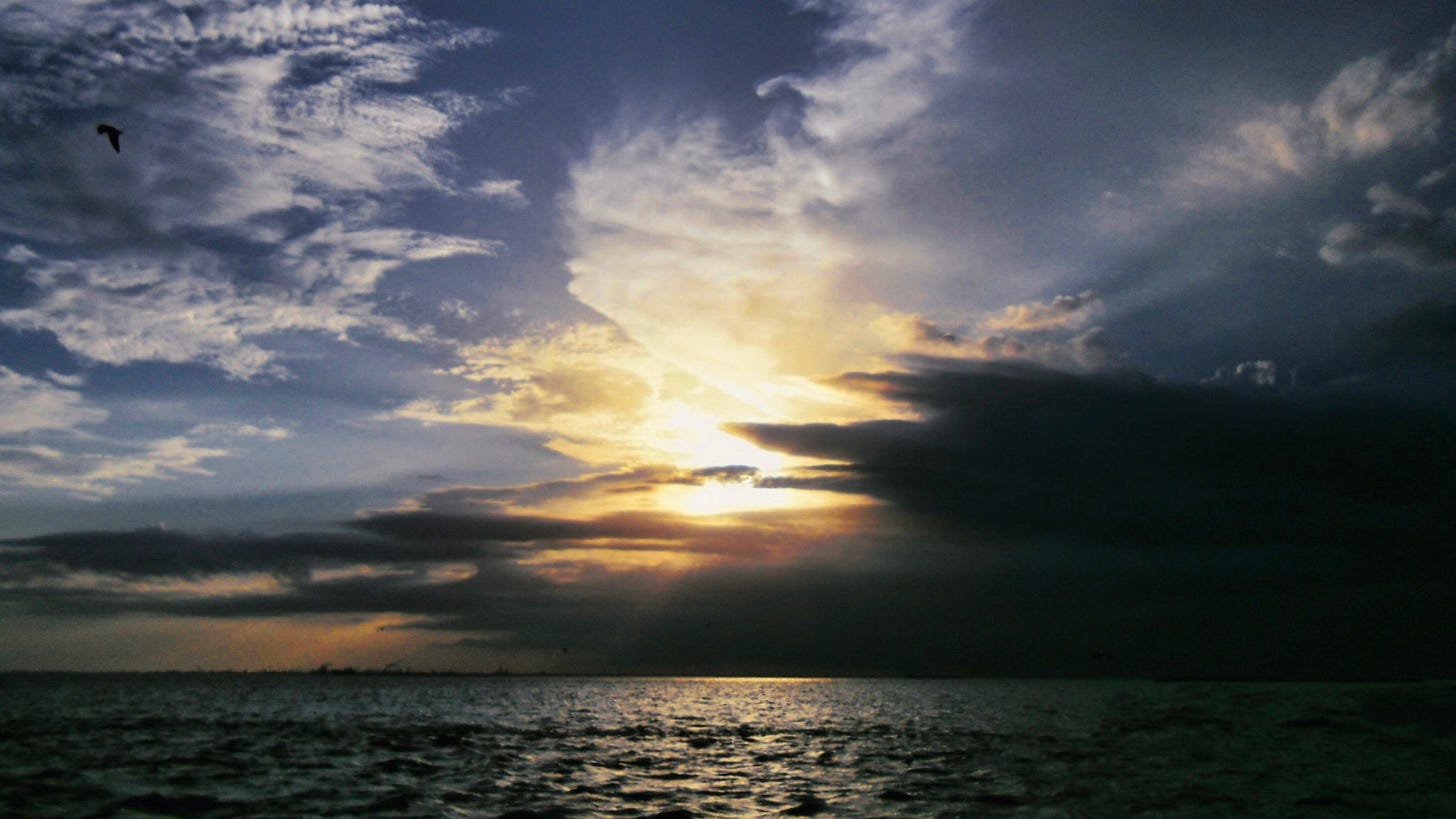 A view of the ocean at sunset with the last rays of sun hidden by clouds against the last remains of blue sky