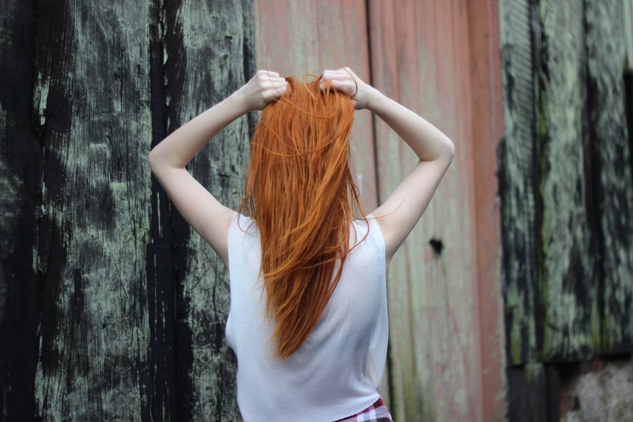 Back view of woman grabbing her orange hair while standing in front of wood panels.