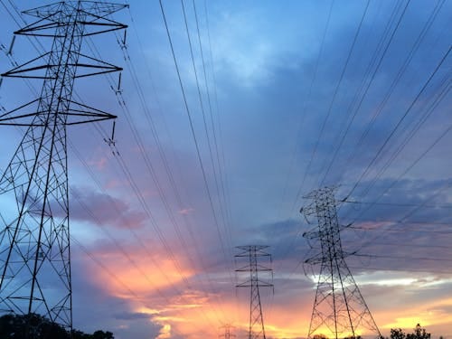 Free A scenic view of high voltage power lines silhouetted against a vibrant sunset sky. Stock Photo