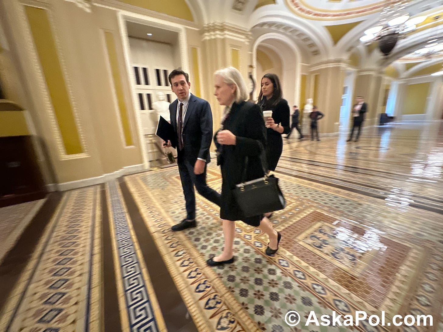 Alady in a power suit walks on marble to a meeting as aides brief her on agenda Photo: Matt Laslo © AskaPol.com