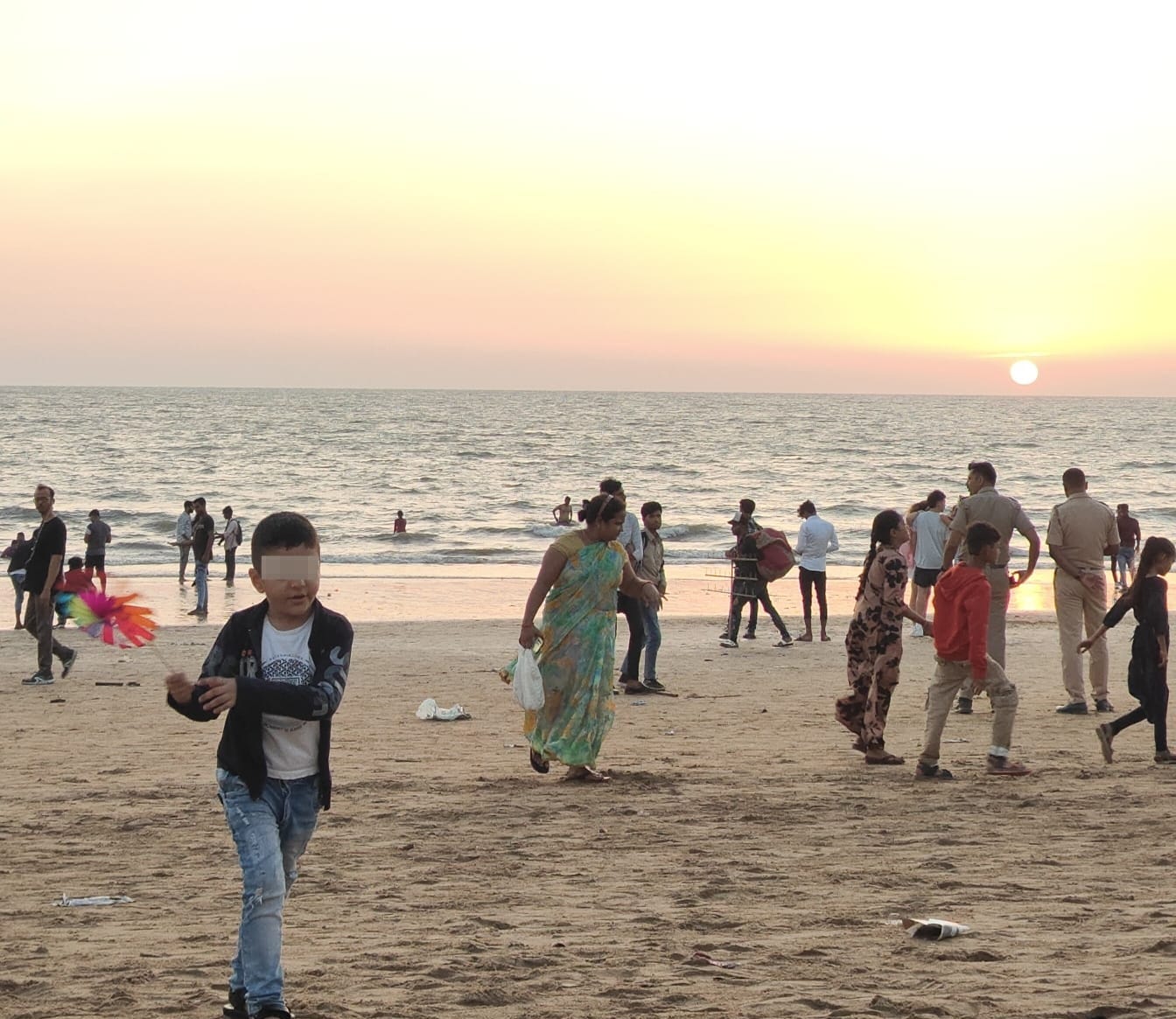 Sunset at a busy beach with children and adults in motion in the foreground, against the backdrop of the sea.
