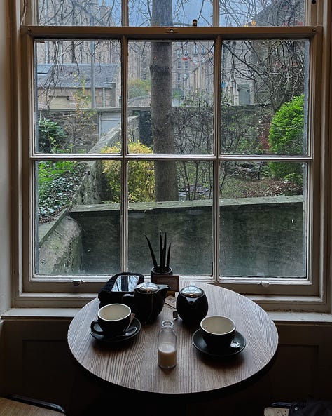 Image 1 - Window display at Twelve Triangles bakery, showing an array of baked goods in warm lighting. / Image 2 - Snowy scene from Princes Street in Edinburgh, with snow blanketing the street and Edinburgh Castle in the background. / Image 3 - Towering sequoia trees at the Royal Botanic Garden. / Image 4 - Table at Grow Urban café with two empty tea cups and a view through the window of greenery outside. / Image 5 - Autumnal overhead shot of my feet stepping on a bed of colourful fallen leaves. / Image 6 - Exhibit display at the Stills Salon exhibition, showcasing framed photography in a minimalist gallery space.