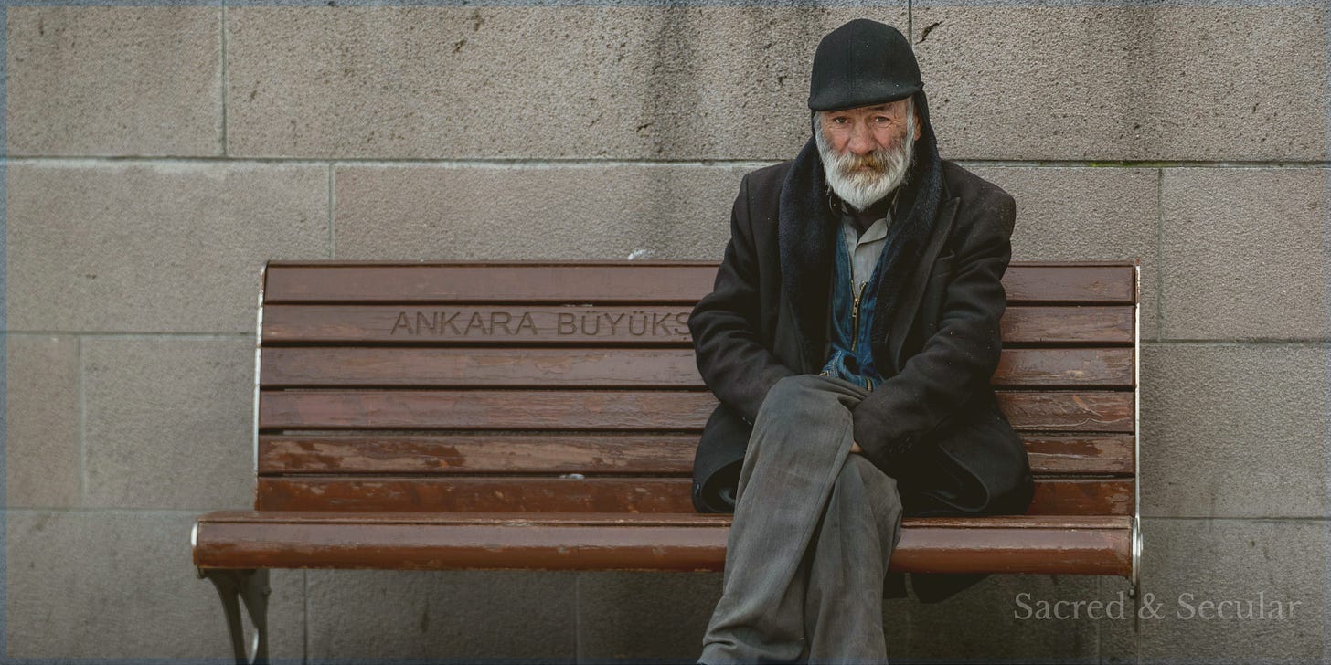 A person sits alone at one end of a wooden bench against a stone wall, leaving much of the bench empty. The quiet, contemplative scene evokes reflection, distance, and the choice between observing life and stepping into it.