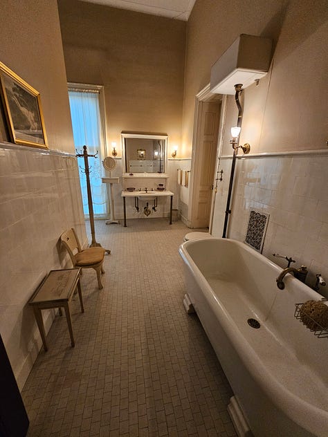 An ornate bedroom with red carpet and gold curtains, and a bathroom with original fixtures.