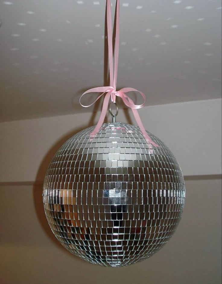 This may contain: a mirror ball hanging from the ceiling with a pink ribbon on it's end