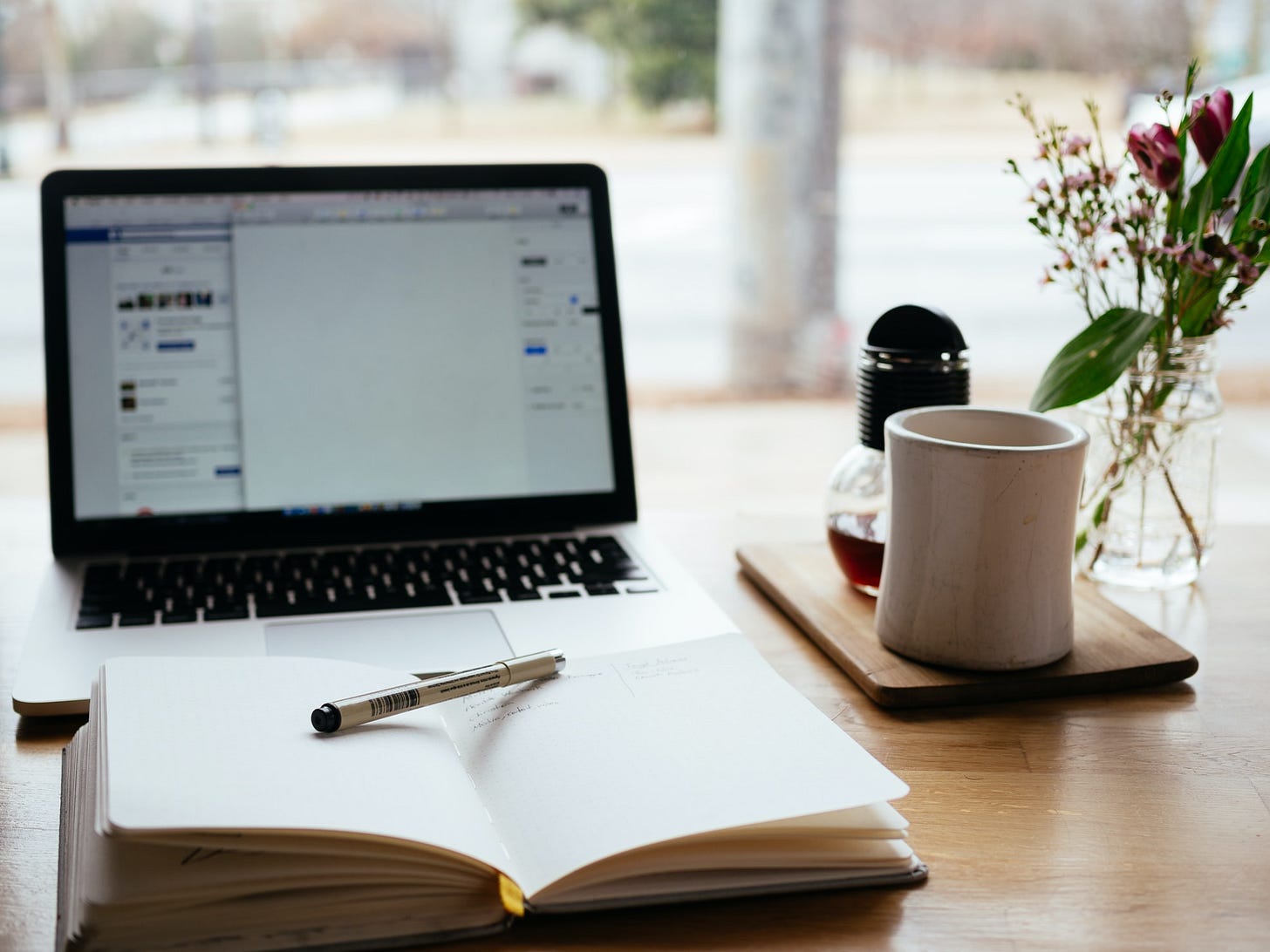 Diario con boli, portátil, café y plantita sobre mesa de madera con luz nórdica. Diario con boli, portátil, café y plantita sobre mesa de madera con luz nórdica.