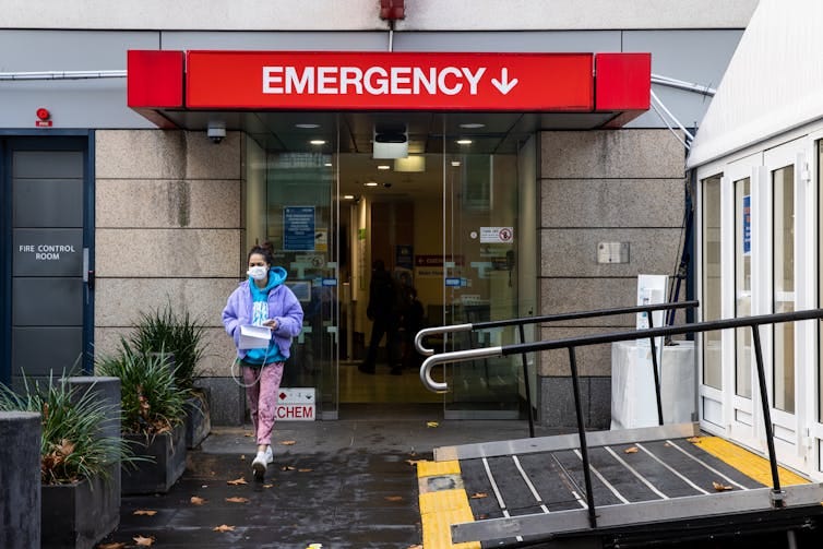 A woman wearing a mask walks out of a hospital. A woman wearing a mask walks out of a hospital.
