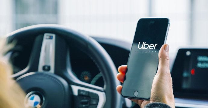Uber driver holding smartphone in car. Uber is an American company offering different transportation services online Uber driver holding smartphone in car. Uber is an American company offering different transportation services online