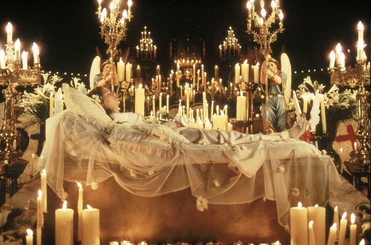 This may contain: a man and woman laying on top of a bed surrounded by candles in front of a chandelier
