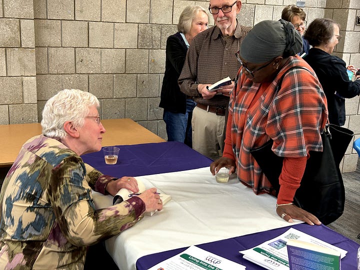 Four photos: a cake with a book cover on it, me at the podium, a crowd scene, and me autographing a book