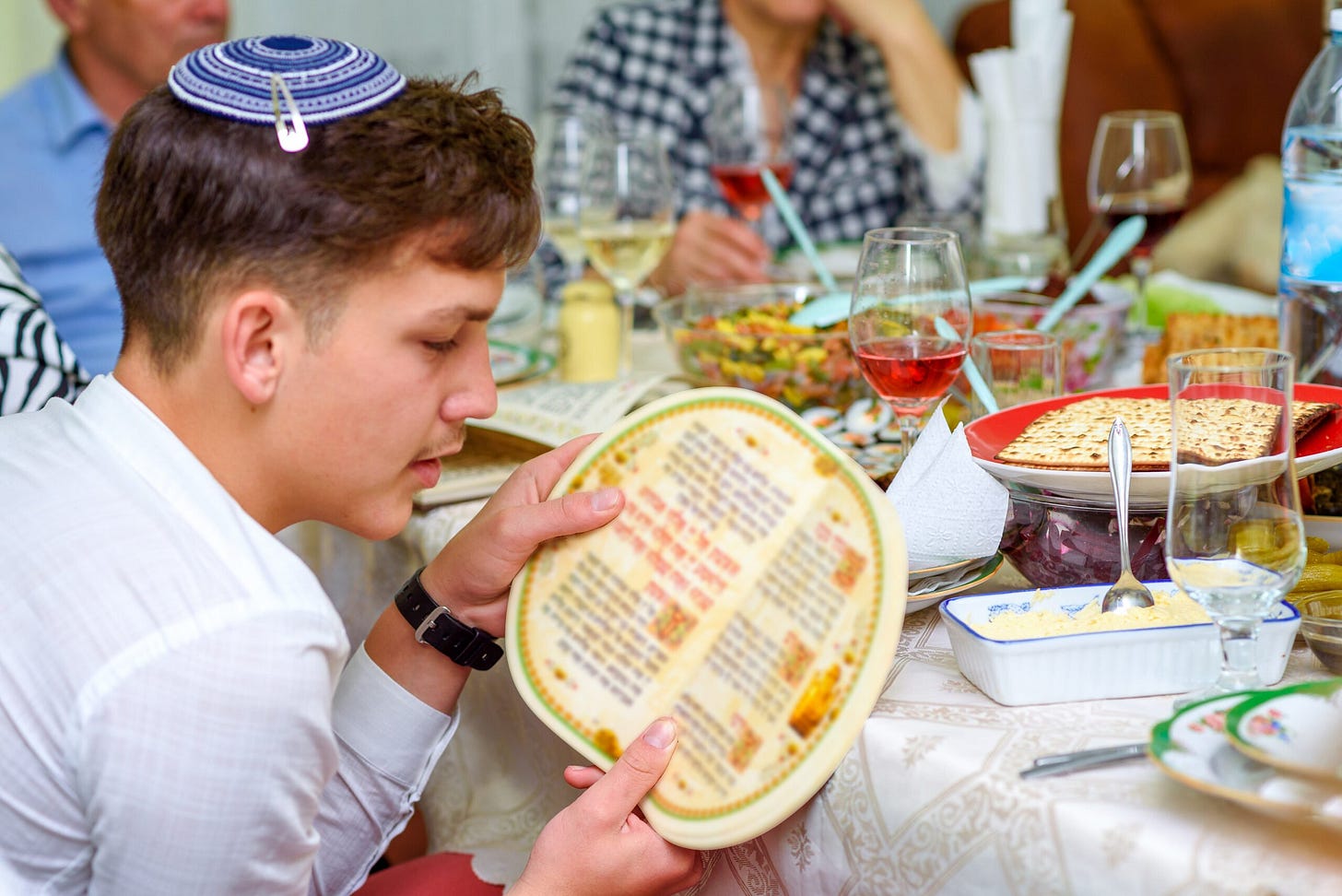 Jewish family celebrate Passover Seder. Young boy with kippah reads the Passover Haggadah.