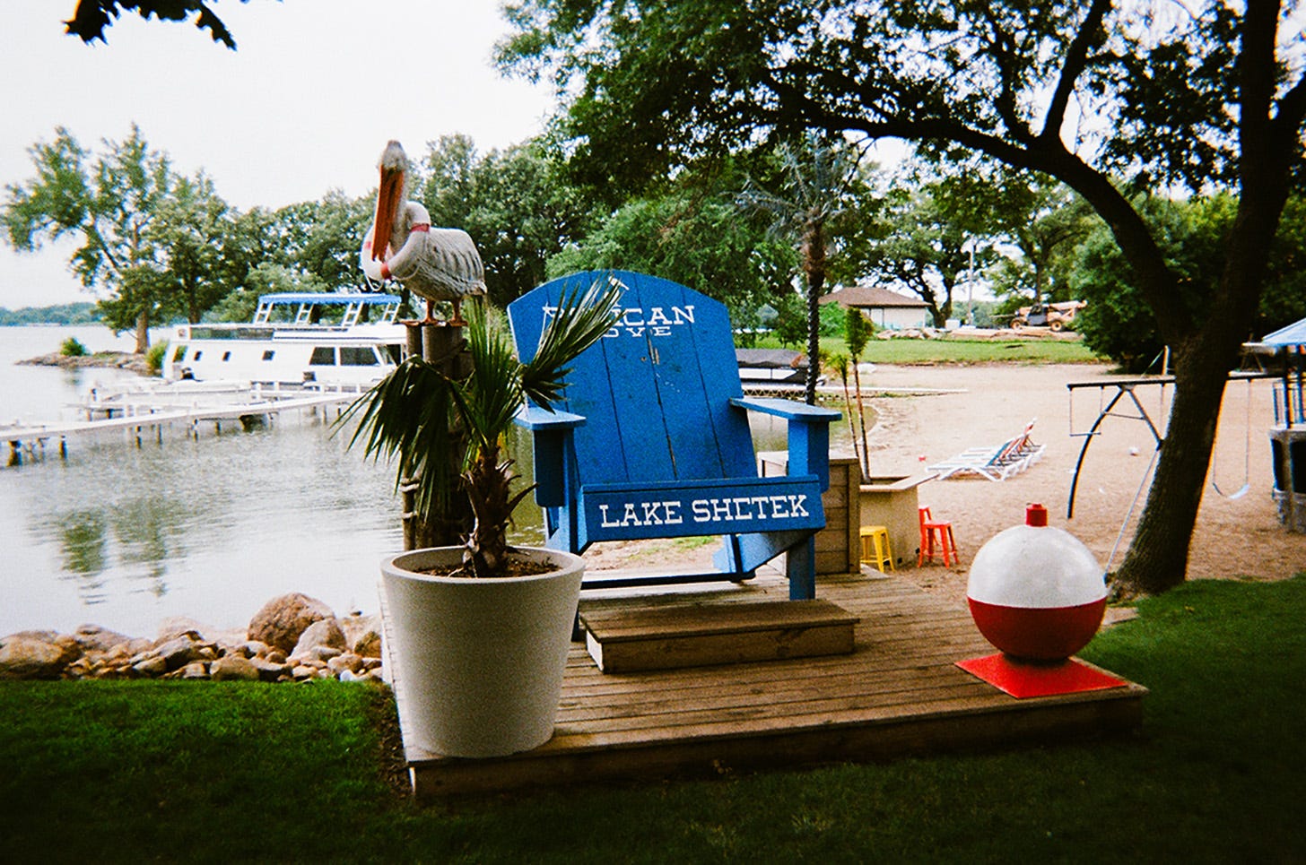 A photo-op: a large blue Adirondack chair with PELICAN COVE LAKE SHETEK written on it surrounded by a pelican, life bouys, palm trees, and fishing bobbers.