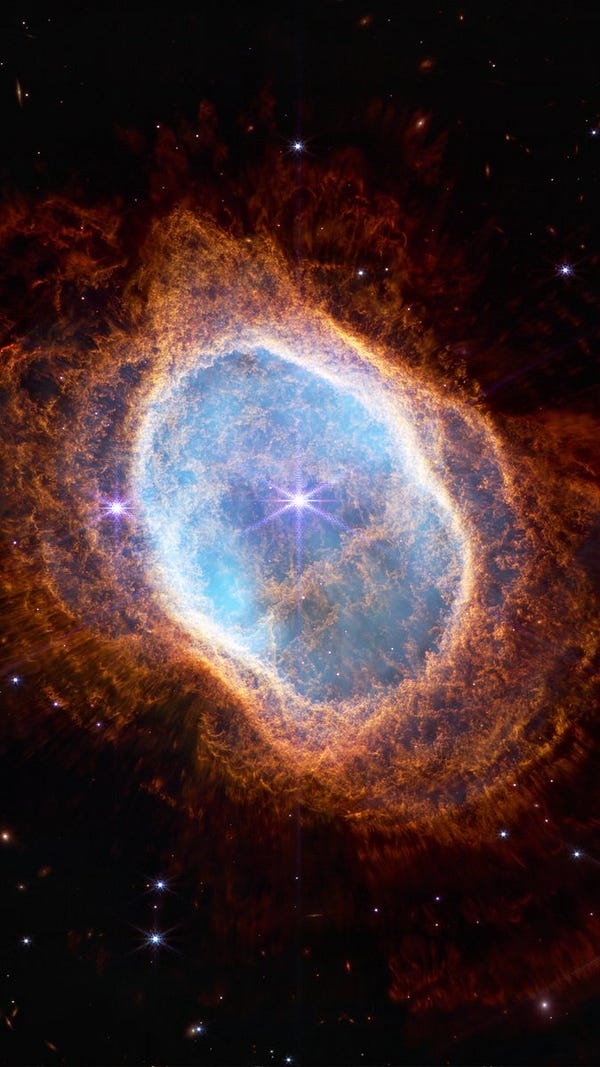 The image is of the Southern Ring Nebula. The background is black and speckled with tiny bright stars and distant galaxies. The nebula is shown as a misshapen oval that is slightly angled from top left to bottom right and takes up the majority of the image. The near-infrared image shows a bright white star at the center with long diffraction spikes. Large, transparent teal and orange ovals, which are shells ejected by the unseen central star, surround it.