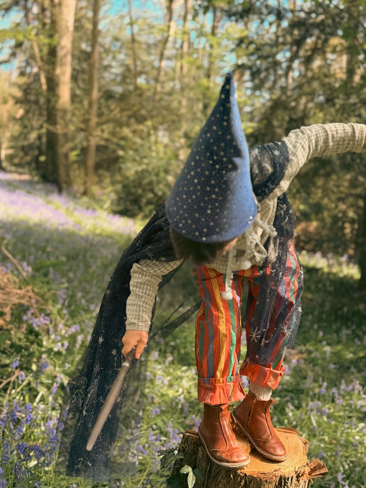 Boy in wizard costume bowing deeply beside girl in fairy costume holding wildflowers in a bluebell forest