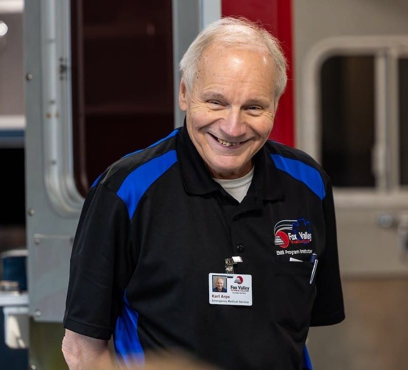 A gray-haired man in a blue and back uniform smiles