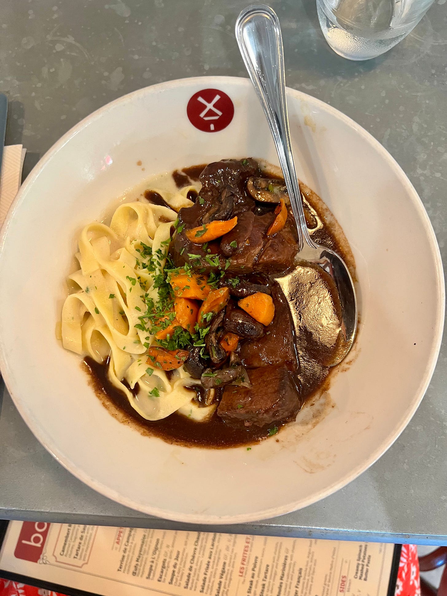 A bowl of boeuf bourguignon at Bouillon by Moulin, tender braised beef with mushrooms and carrots over tagliatelle pasta in a rich red wine sauce.