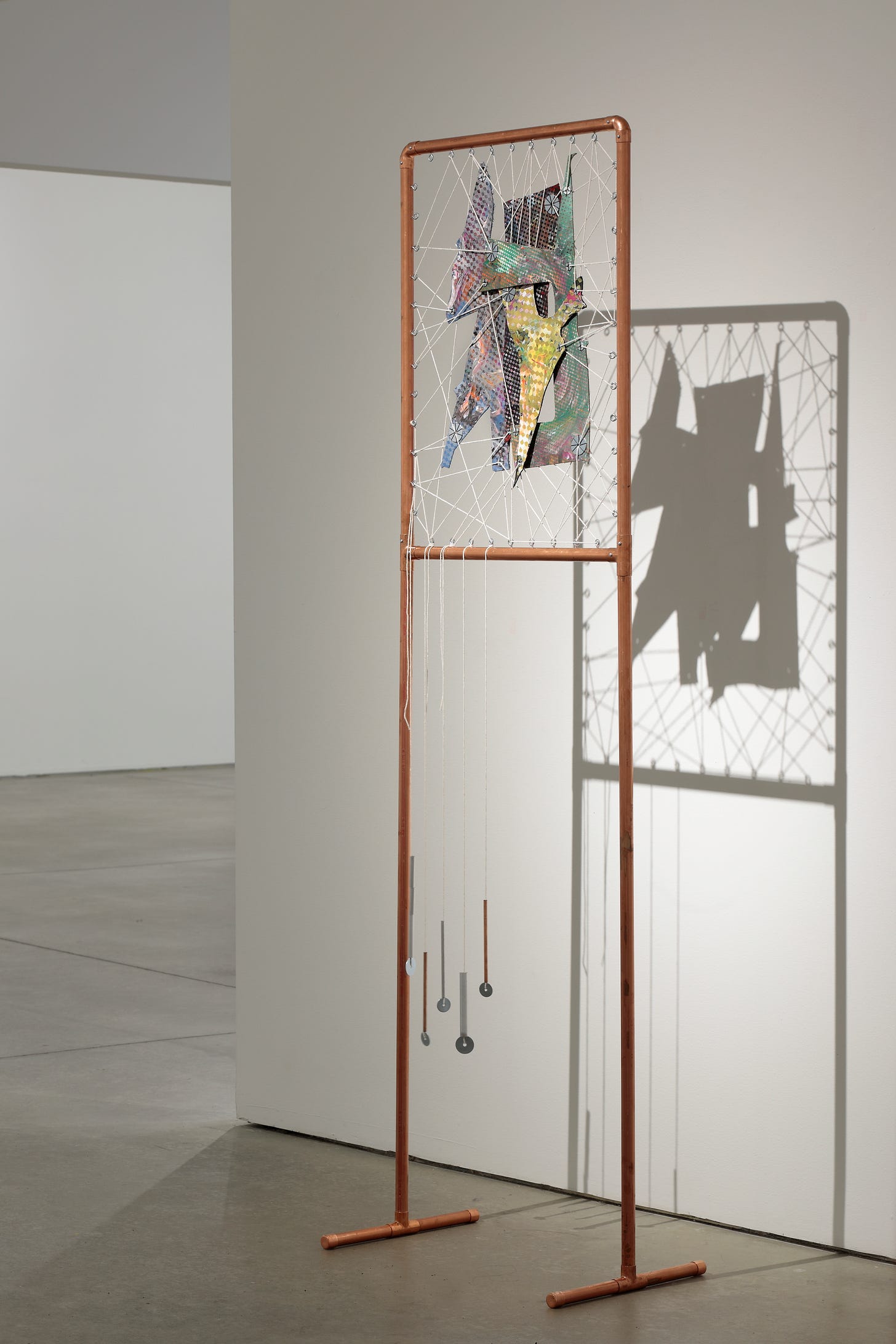 Copper frame with scraps of painted leather suspended inside the copper frame using cotton twine. The painting casts a shadow on the white wall. Copper frame with scraps of painted leather suspended inside the copper frame using cotton twine. The painting casts a shadow on the white wall.