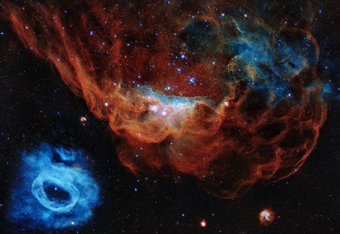 An image of two prominent nebulae within the Large Magellanic Cloud. The upper portion features a large, reddish nebula with intricate, wispy structures and scattered bright blue stars, indicating regions of active star formation. The lower left shows a smaller, bright blue nebula with a ring-like shape. The contrast between the red and blue hues highlights the different types of gases and star-forming activities within these regions. The dark background is dotted with numerous stars, adding depth to the image.