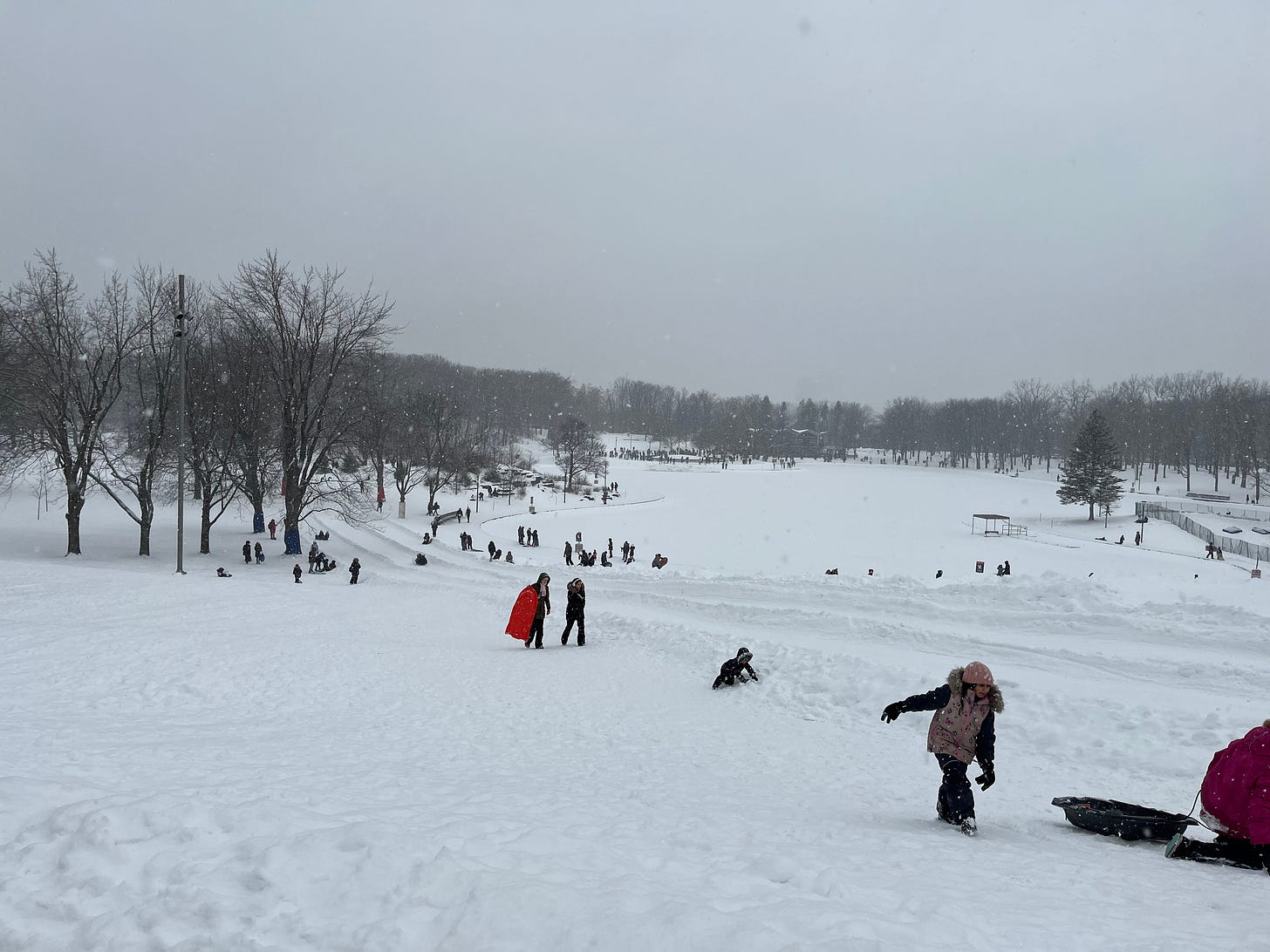 View of several bundled people sledding in a snowy landscape. The figures are scattered across the landscape, as in Breughel paintings.